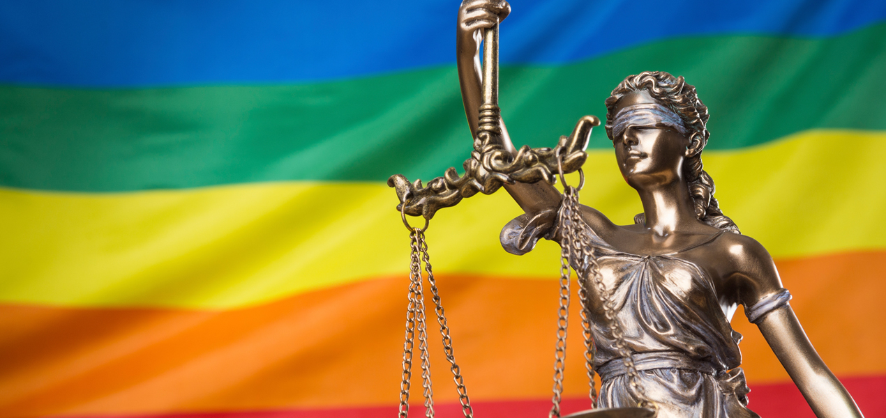 A statue of Justice against a rainbow flag.